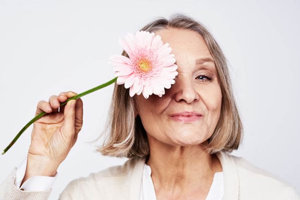 Mulher madura sorrindo com uma flor sobre um dos olhos, representando o climatério e a menopausa