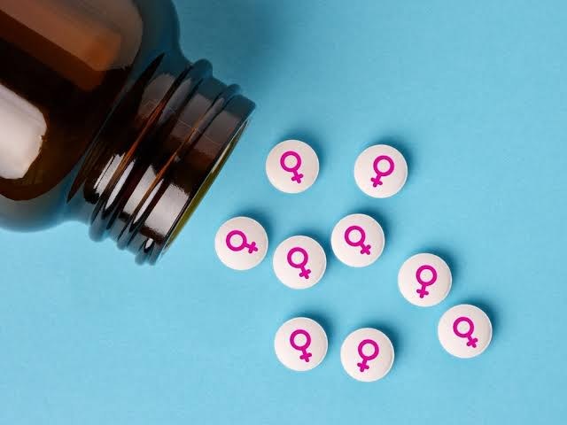 Frasco e comprimidos com o símbolo feminino sobre fundo azul, representando os tratamentos não hormonais